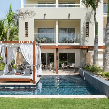 Dreams Royal Beach Punta Cana (Adults Only) Exterior photo Captured on a bright, sunny day, this medium shot showcases a luxurious resort setting. The focal point is a sleek, modern building, likely a hotel or villa, painted in a warm beige. It features multiple levels, each with large glass doors leading to