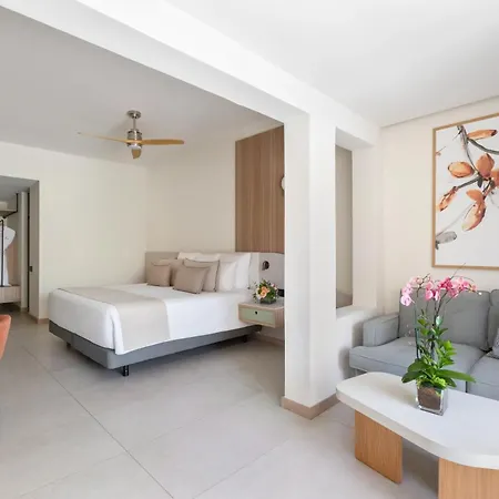 Dreams Royal Beach Punta Cana (Adults Only) Room photo The photo shows a modern and airy hotel room with a combined bedroom and living area. The color palette is predominantly white and light beige, creating a bright and spacious feel. 

In the foreground, a comfortable light gray sofa with decorative pi
