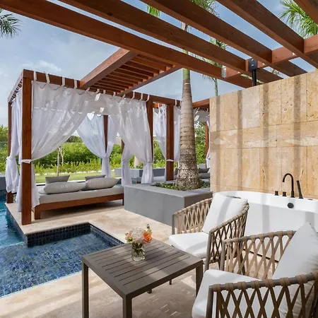 Dreams Royal Beach Punta Cana (Adults Only) Amenities photo The photo shows a luxurious outdoor relaxation area, likely part of a resort or high-end home. The main feature is a freestanding, oval-shaped bathtub situated against a textured, light brown wall with vertical seams. A sleek, black faucet is mounted