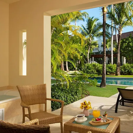 Dreams Royal Beach Punta Cana (Adults Only) Amenities photo The photo shows a luxurious outdoor seating area, likely part of a hotel or resort, with a stunning view of a tropical landscape. The area is partially covered by a light-colored overhang, providing shade. 

In the foreground, there are two wicker ar
