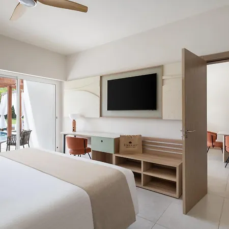 Dreams Royal Beach Punta Cana (Adults Only) Room photo The photo shows a modern hotel room with a clean and bright aesthetic. The room features a large bed with white linens and a light beige throw. A flat-screen TV is mounted on the wall above a light-colored desk area with shelves and drawers, providin