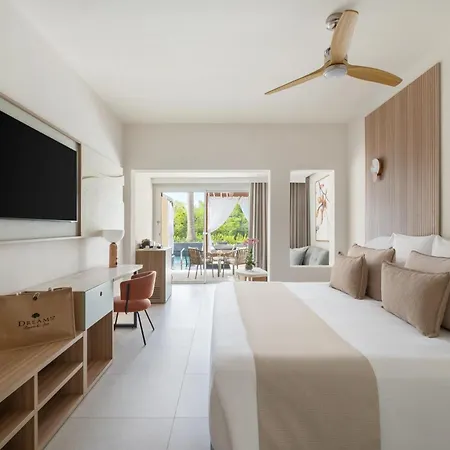 Dreams Royal Beach Punta Cana (Adults Only) Room photo The photo shows a bright and modern hotel room with a focus on a comfortable bedroom area. 

The room features a large bed with crisp white linens and several plush pillows in shades of beige and brown. A light beige runner is placed across the foot 