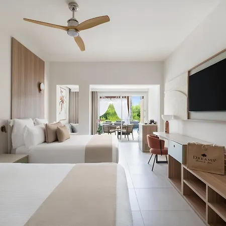 Dreams Royal Beach Punta Cana (Adults Only) Room photo The photo shows a bright and airy hotel room with a modern and minimalist design. The room features two double beds with white linens and light beige throws. Each bed has multiple pillows, including some in a textured beige fabric. 

The walls are pa